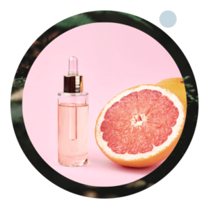 Eine halbierte Grapefruit mit der angeschnittenen Seite nach oben, daneben ein kleines, transparentes Fläschchen mit Grapefruitöl.